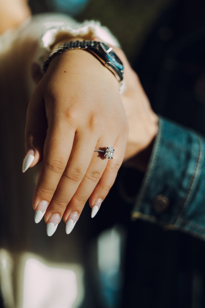 Close-up of a manicured hand showcasing a sparkling diamond ring in natural lighting.